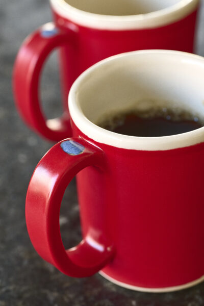 Red ceramic mug with a blue dot on top of the handle filled halfway with coffee