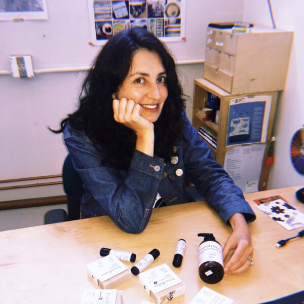 Alana Rivera with right hand resting on chin and left hand touching Etta + Billie products on a table.