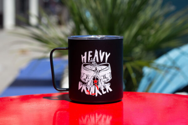 A black camp mug that says "heavy drinker" on a red table